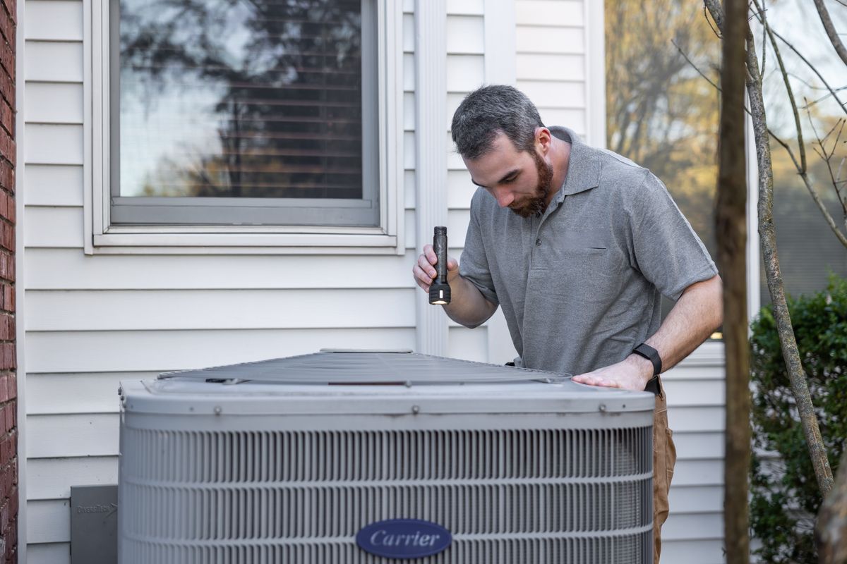 An HVAC technician inspecting an outdoor air conditioner condenser to decide whether to repair or replace it